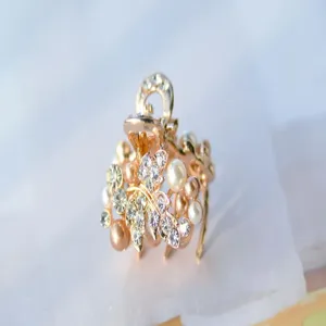 Close-up detail of a golden mini hair claw clip decorated with sparkling rhinestones and pearls.
