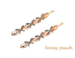 Gros plan detail de la pince a cheveux doree en strass, design cristal peche etincelant.
