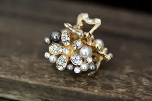 Close-up detail view of a mini golden hair claw clip decorated with sparkling rhinestones and pearls.