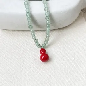 Close-up detail of aventurine green bead necklace featuring a vibrant red gourd pendant.