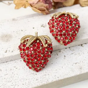 Detailed close-up of retro red rhinestone strawberry brooch and earrings set, golden leaf accent.