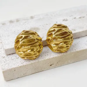 Close-up of vintage textured gold metal earrings on stone. Detailed metallic surface design.