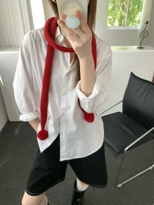 Detailaufnahme des roten, schmalen Strickschals mit verspielten Bommeln, lässiger Look.