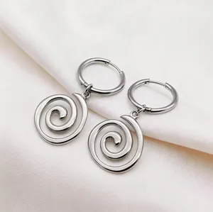 Close up detail of silver stainless steel spiral pendant hoop earrings on white soft fabric.