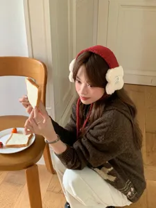 Close-up detail of the plush winter earmuffs in red and white worn by model indoors.