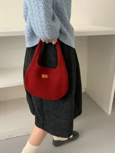 Close-up detail of the red knitted underarm bag, soft fabric texture and leather label.