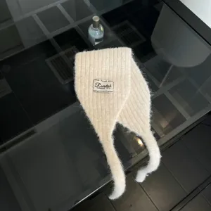 Detailaufnahme des weichen, cremefarbenen Strick-Schals mit Bändern und gemütlichen Ohrenschützern.