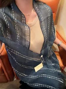 Detailansicht eines dunkelblauen Leinenschals mit weißen Streifen und Fransen am Model.