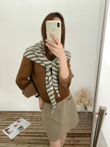 Detail view of a stylish striped knit triangular shawl paired with a chic brown suede jacket.