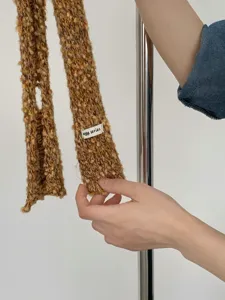 Primo piano della sciarpa stretta marrone in maglia, che mostra la sua trama tweed e dettagli in lana.