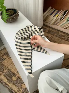 Close-up detail of a chic black and white striped knit triangle scarf with metal accent.