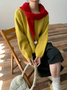 Dettaglio che mostra un accogliente cardigan giallo in maglia e una sciarpa rossa.