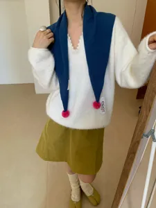 Dettaglio sciarpa triangolare in lana con pon pon colorati per un caldo stile invernale.