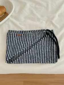 Primo piano di sciarpa triangolare a righe in maglia con lacci e dettaglio di etichetta in pelle.