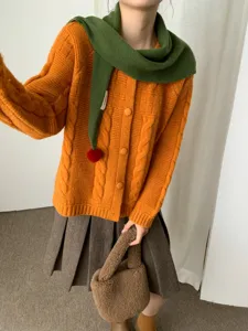 Dettaglio di cardigan in maglia arancione da donna con sciarpa a pompon verde e gonna invernale.
