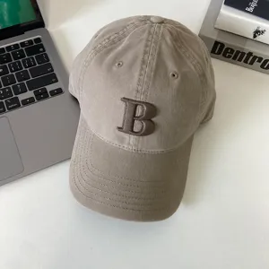 Detailaufnahme der beigen Baseballkappe mit auffallender gestickter Buchstabenstickerei.