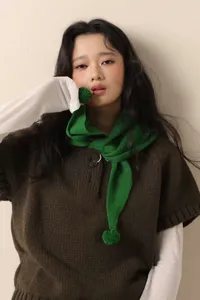 Green knitted triangular scarf detail with cute pom-pom, soft winter neck warmer accent.