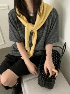 Detailed view of a stylish yellow knitted hollow-out scarf draped over a striped top.