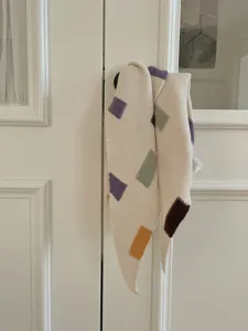 Detalle de bufanda triangular de punto con bloques geométricos de colores y etiqueta de lavado.
