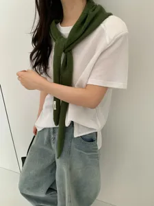 Detailed shot of a stylish dark green knit scarf draped over a white t-shirt and jeans.