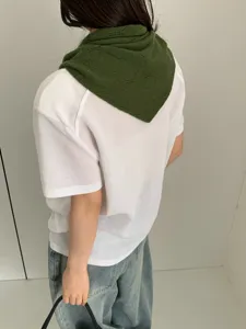 Detail view of a green knit hollow triangular scarf worn on a model, showcasing texture.
