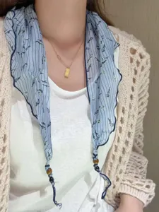 Close-up of lightweight floral print neck scarf with beaded ends, elegant styling detail.