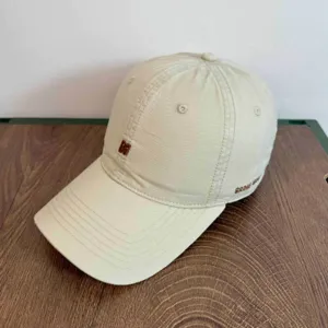 Vista detallada de gorra de béisbol de algodón beis con letra N bordada y texto lateral, estilo casual.