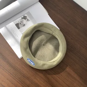 Primer plano de una boina de punto caqui con pequeña etiqueta azul sobre madera.