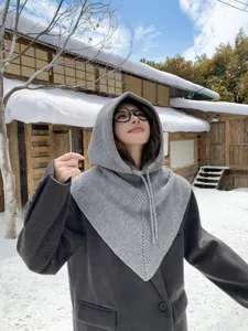 Vue détaillée de la cagoule en tricot gris avec capuche et écharpe dans la belle neige.