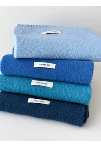 Detailed view of stacked knitted wool scarves in blue shades with 100% wool product tags.