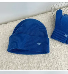 Blue knit beanie and mittens set detail shot showing soft ribbed texture and metal badge.