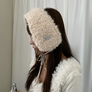 Nahaufnahme der flauschigen Winter Plüsch Ohrenklappen Mütze in Beige mit süßen Bändern.