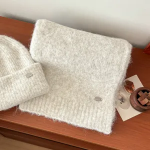Conjunto de gorro y bufanda de punto suave en beige, con elegantes etiquetas metálicas.