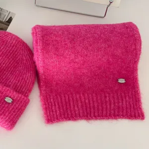 Vista detallada de conjunto de gorro y bufanda de punto rosa brillante con textura suave y metal.