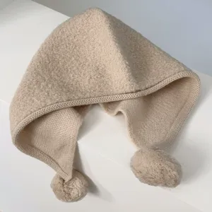 Close-up of cozy beige knit balaclava with cute pom-poms and earflaps for winter warmth.