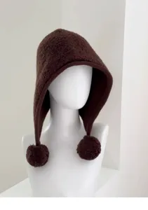 Close-up detail of the brown knit balaclava hat showing soft wool texture and cute pom-poms.