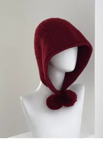 Closeup of a dark red knitted balaclava hat with cute pom-pom strings, soft wool texture.