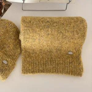 Vista detallada del conjunto de bufanda y gorro de punto amarillo suave con logo metálico.