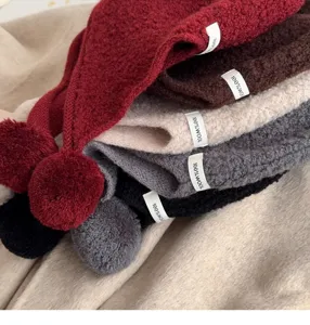 Close-up detail of cozy knit wool balaclava hats with cute pom-poms in various colors.