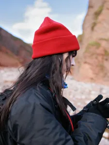 Close-up detail of a bright red knit cuffed beanie hat worn in an outdoor rocky mountain setting.
