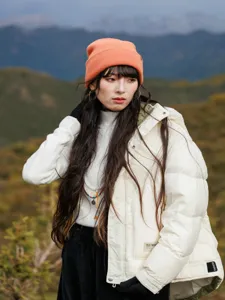 Outdoor detail shot of warm orange knit beanie hat worn by model in scenic mountain landscape.