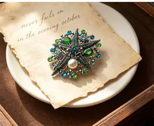 Close-up detail of vintage starfish brooch with green blue crystals and pearl on aged paper.