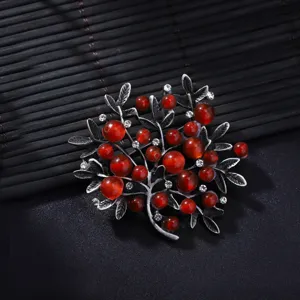 Detailed close-up of retro tree branch brooch, featuring red stones and antique silver leaves.