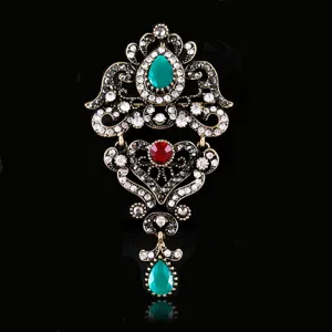 Close-up of vintage baroque brooch, ornate gold-tone metal with green and red crystal rhinestones.