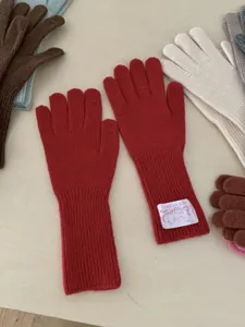 Detailaufnahme roter Strickhandschuhe mit verlängertem Rippbündchen und gewebtem Markenetikett.