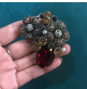 Detailed view of vintage crystal rhinestone floral brooch with red glass gem pendant.