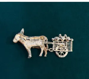 Close-up detail of a vintage gold-toned donkey pulling a cart brooch, metal alloy jewelry.