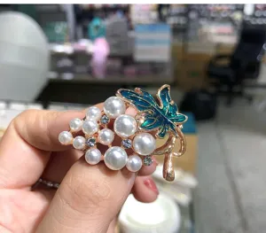 Close-up of exquisite grape brooch featuring shiny pearls, rhinestones, and blue enameled leaf detail.
