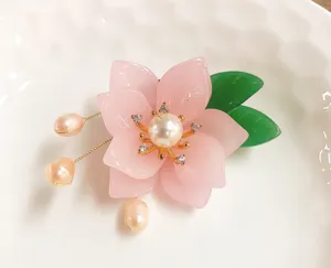Exquisite pink flower brooch with pearl stamens and green leaves, delicate detail shot accessory.
