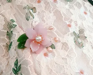 Close-up of pink translucent flower brooch with pearl details on delicate lace fabric.
